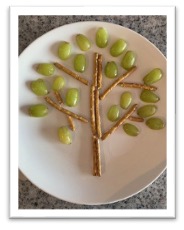 a plate with stick pretzels and grapes arranged to look like a tree