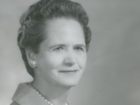 Black and white image of Carolyn Field dressed in a suit with pearl earrings and a pearl necklace.